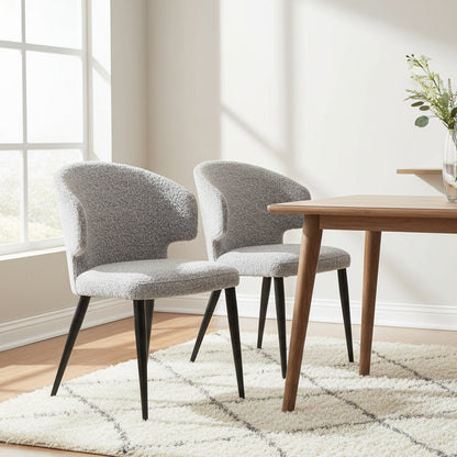 The Baker Pair of Belle Dining Chairs are upholstered in a light Grey Boucle fabric, with black powder coated legs, and a curved backrest
