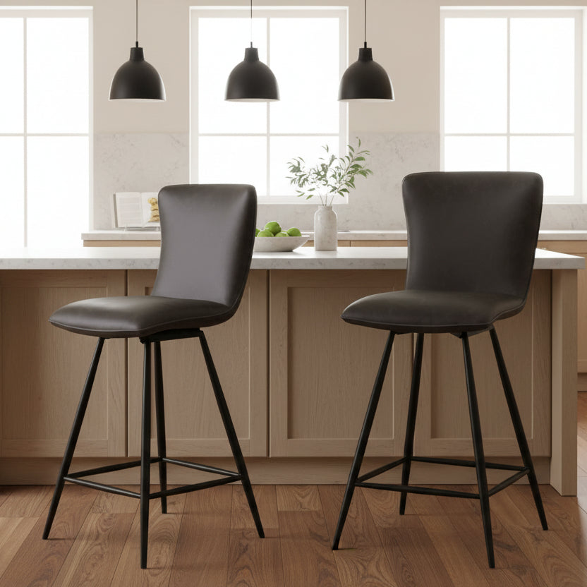 The Baker Pair of Ella Bar Chairs are upholstery in a Dark Grey faux leather fabric, with 180 degree swivel seats and black metal legs with footrest bar