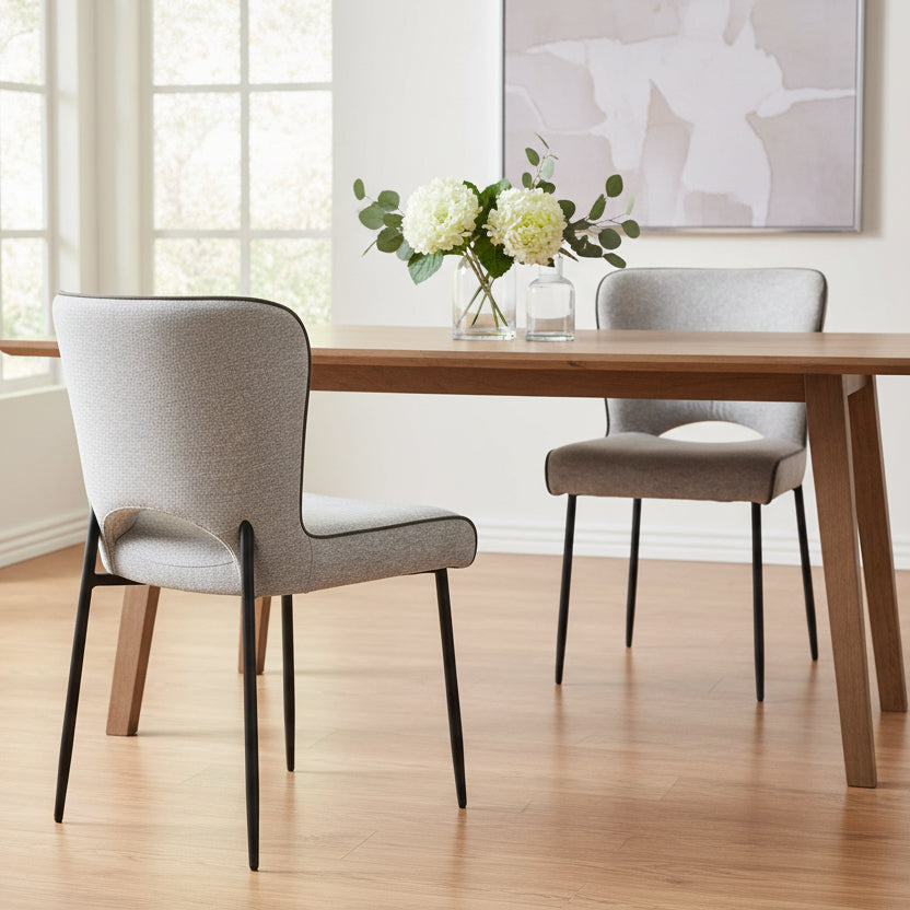 The Baker Pair of Maya Dining Chairs upholstered in Light Grey linen fabric with a contrasting PU leather trim and black metal legs