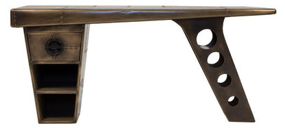 Carlton Furniture Aviator Half Wing Desk in Vintage Brass features an asymmetric wing leg with circular cut-outs and a winged shaped desk top. A top drawer and lower shelving is ideal for storage