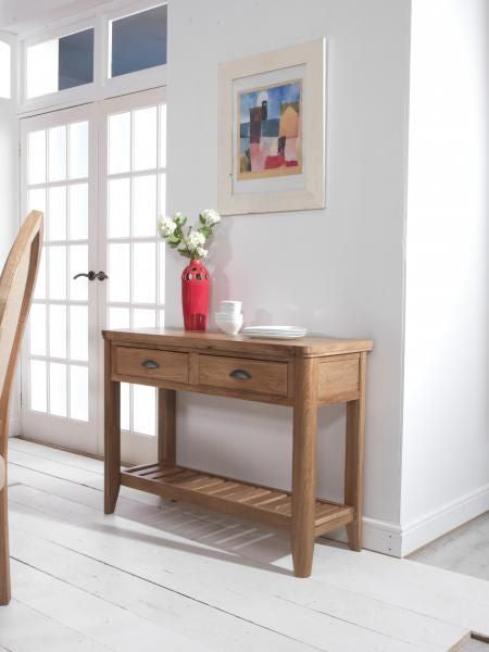 Carlton Furniture Copeland Console Table is crafted from natural solid oak wood and features 2 drawers with metal cup handles, plus a lower shelf for useful storage or display purposes