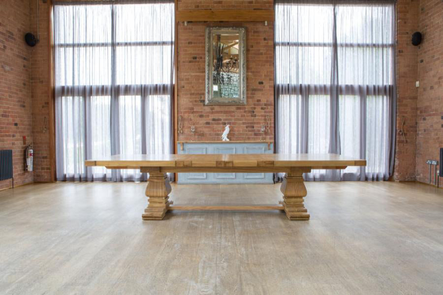 The Carlton Furniture Windermere Rustic Monastery Extending Dining Table is crafted from natural solid oak wood with pedestal legs and a thick table top, seating 12-14 when fully extended