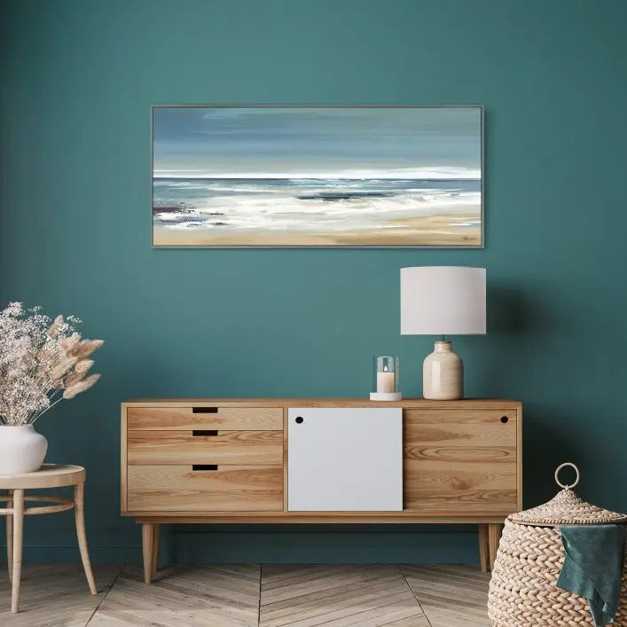 Along the Coastline Framed Canvas by Valerie Mravyan for Gallery Direct depicts a striking seascape of crashing waves against the sandy coastline in a simple palette of blues and greens, complemented by a thin dark grey wood frame
