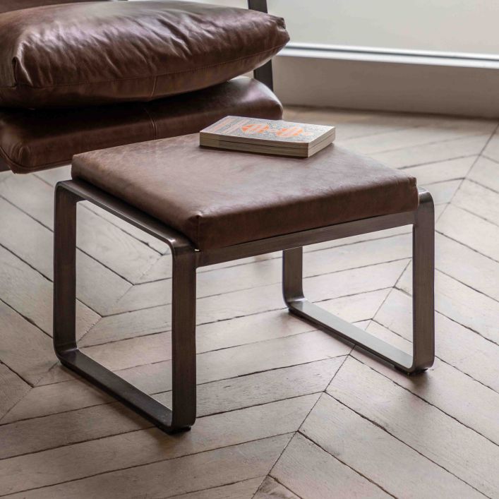 The Gallery Direct Fabien Footstool is upholstered in Brown Leather and has dark metal curved legs