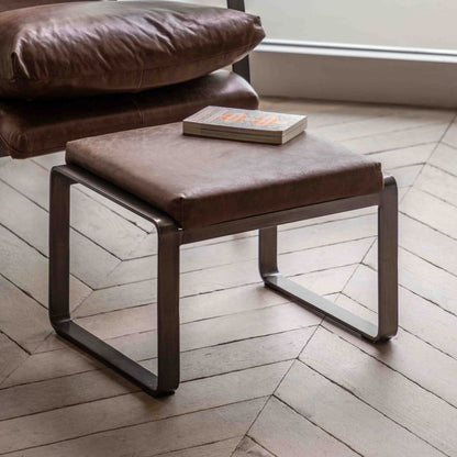 The Gallery Direct Fabien Footstool is upholstered in Brown Leather and has dark metal curved legs