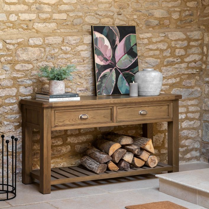 Gallery Direct Hardwick 2 Drawer Console Table is crafted from solid oak and veneers in a warm wood finish, with metal pull handles and a slatted lower shelf