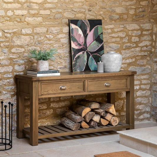 Gallery Direct Hardwick 2 Drawer Console Table is crafted from solid oak and veneers in a warm wood finish, with metal pull handles and a slatted lower shelf