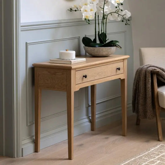 Gallery Direct Malvern Console Table is constructed from premium oak solids and veneers with wood-grain patterns and features 1 wide drawer with metal handles, and slim tapered legs