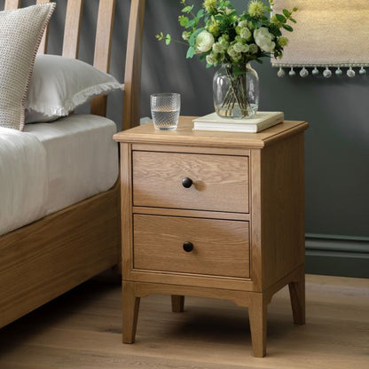 Gallery Direct Malvern 2 Drawer Bedside Cabinet is constructed using warm oak solids and veneers with natural grain patterns, complemented by dark metal handles and with slim tapered legs
