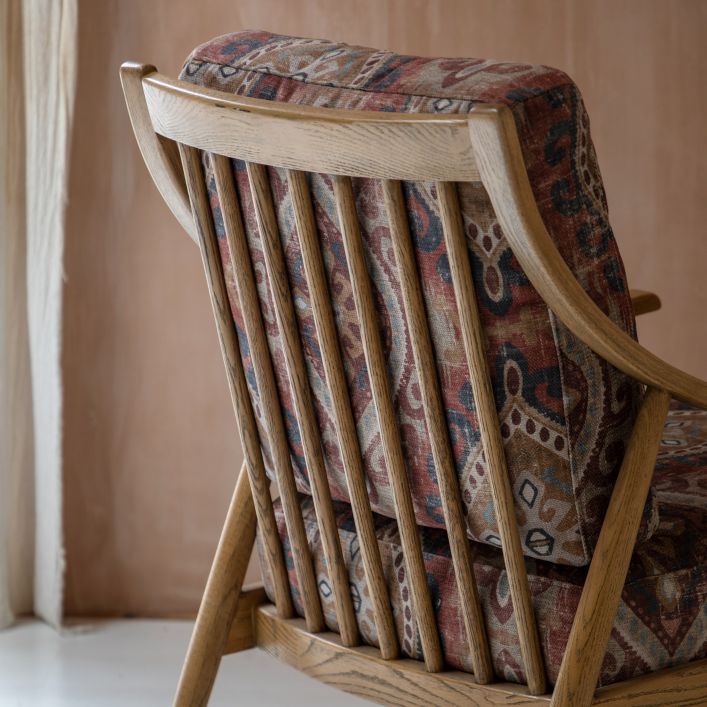 The Gallery Direct Reliant Armchair is crafted from solid ash wood with a spindle backrest and has padded seat cushions in a Zari Jacquard patterned fabric