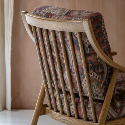 The Gallery Direct Reliant Armchair is crafted from solid ash wood with a spindle backrest and has padded seat cushions in a Zari Jacquard patterned fabric