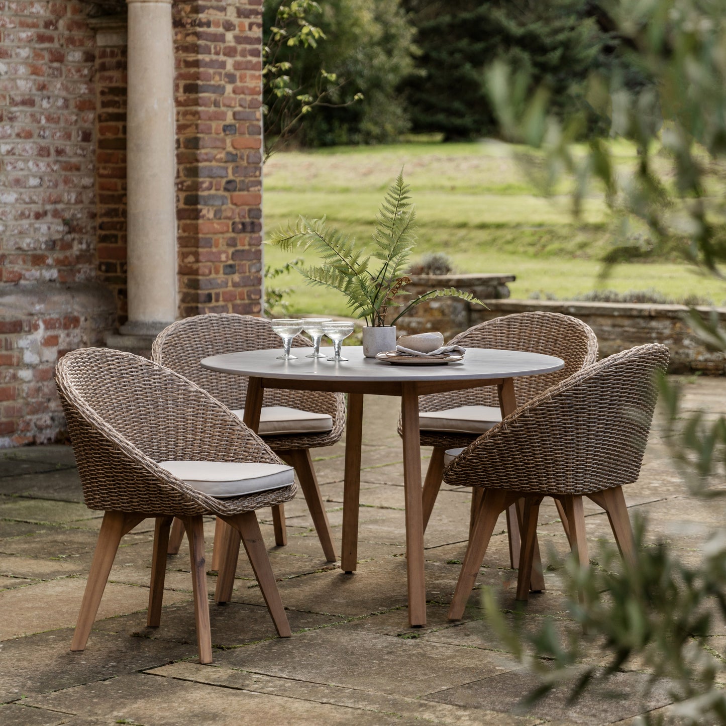 Gallery Garden Avena 4 Seater Round Dining Set features a tempered glass table top, acacia wood legs and 4 woven wicker style chairs with natural coloured seat pads