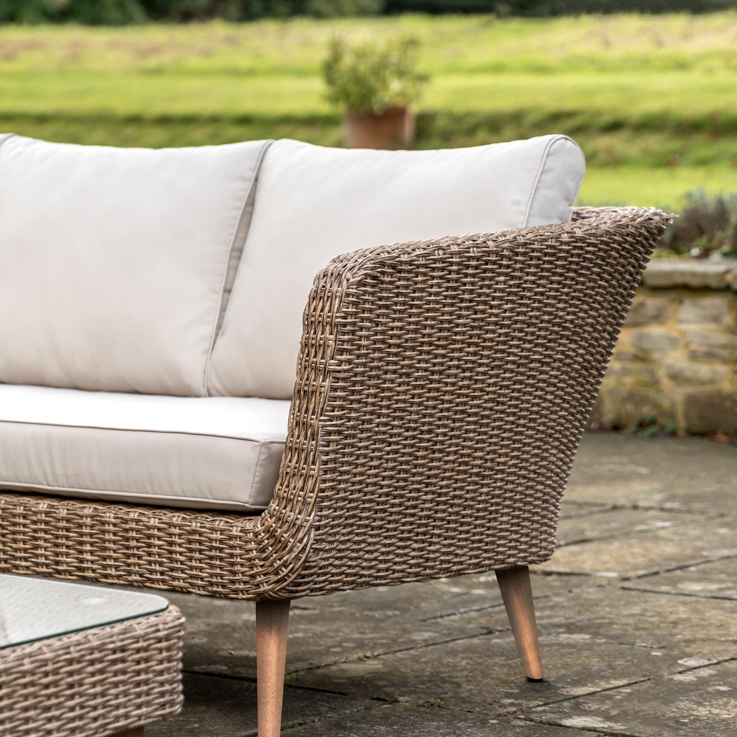 Gallery Garden Avena Corner Lounge Set features a poly-rattan wicker style sofa frame with acacia wood legs and cream padded seat cushions, plus a glass top square coffee table 