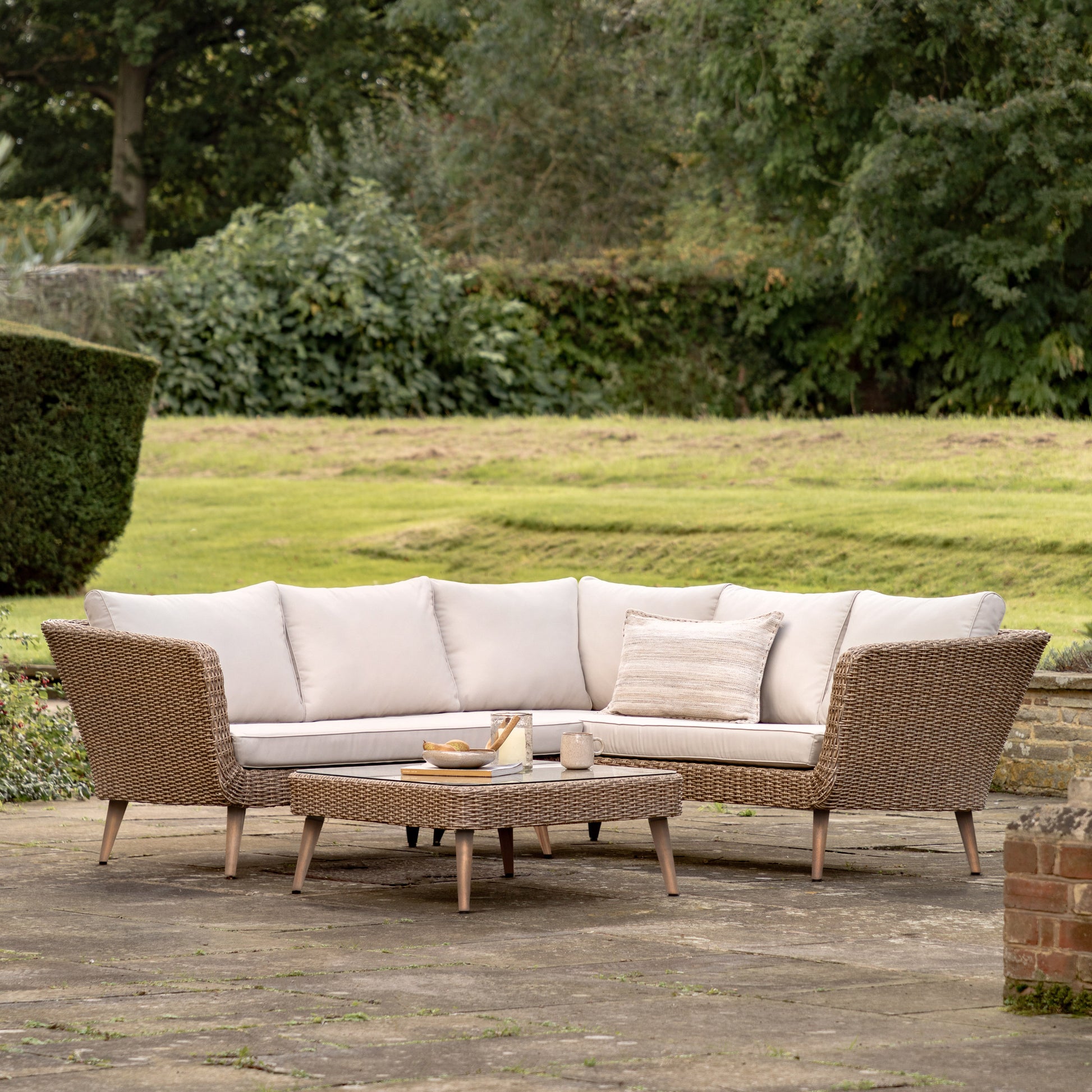 Gallery Garden Avena Corner Lounge Set features a 5 seater corner sofa and a matching glass top coffee table, with poly-rattan wicker frame and generously padded natural toned cushions