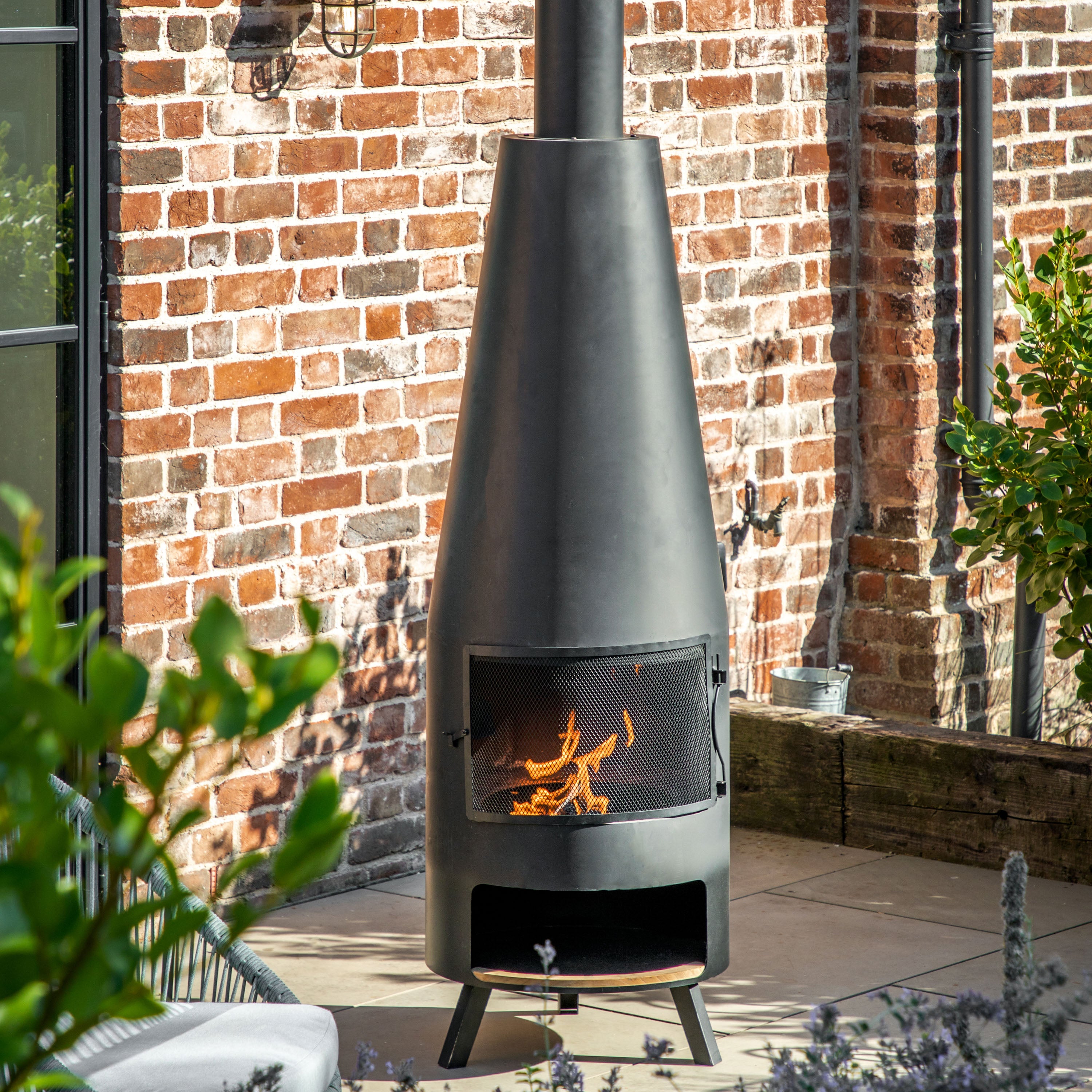 Gallery Garden Foligno Chiminea with Pizza Shelf features a black metal fire chamber with mesh front, elevated flue and lower pizza shelf