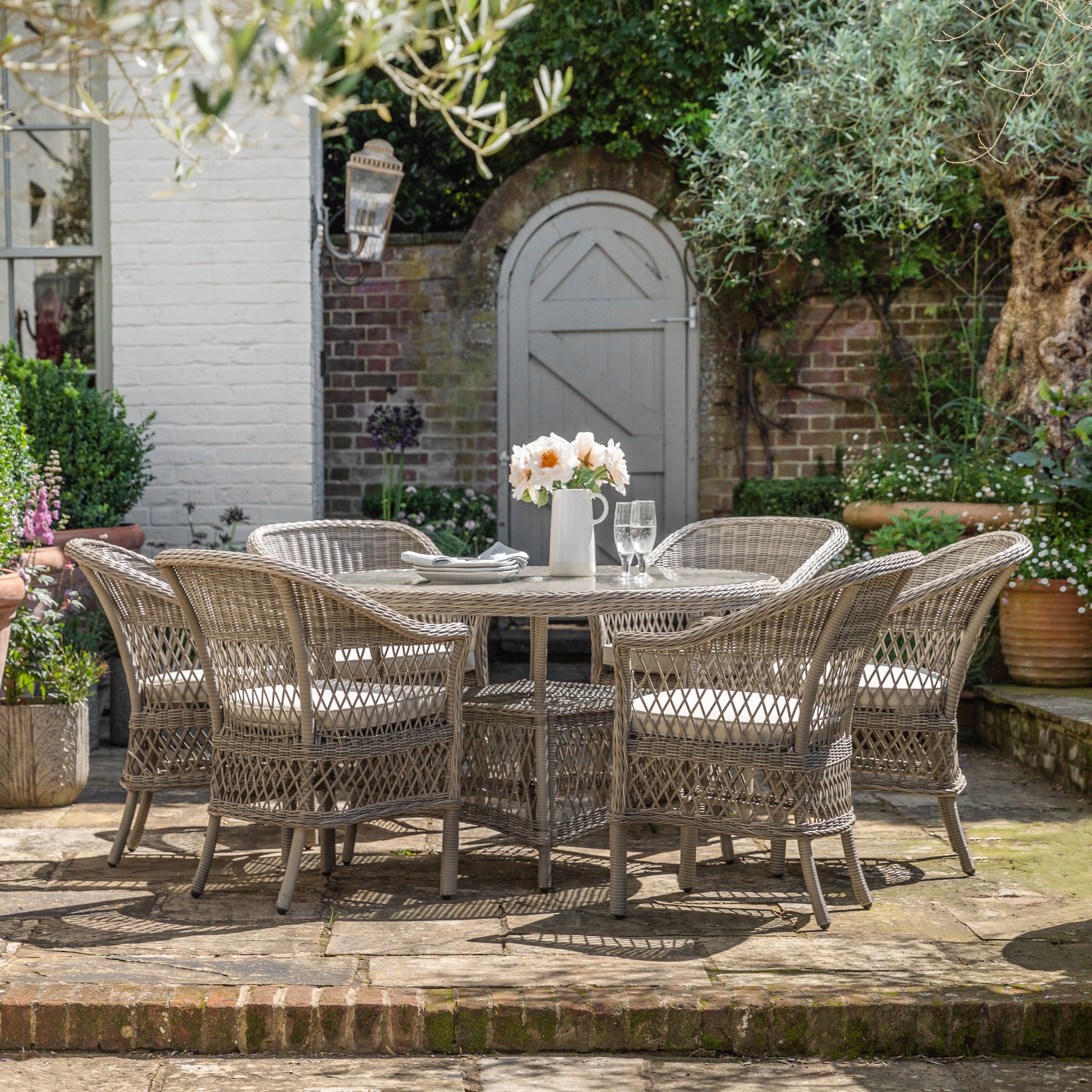 Gallery Garden Menton 6 Seater Round Dining Set features a glass topped table with an underneath shelf constructed in a stone colour PE woven rattan, and 6 matching armchairs with padded seat cushion