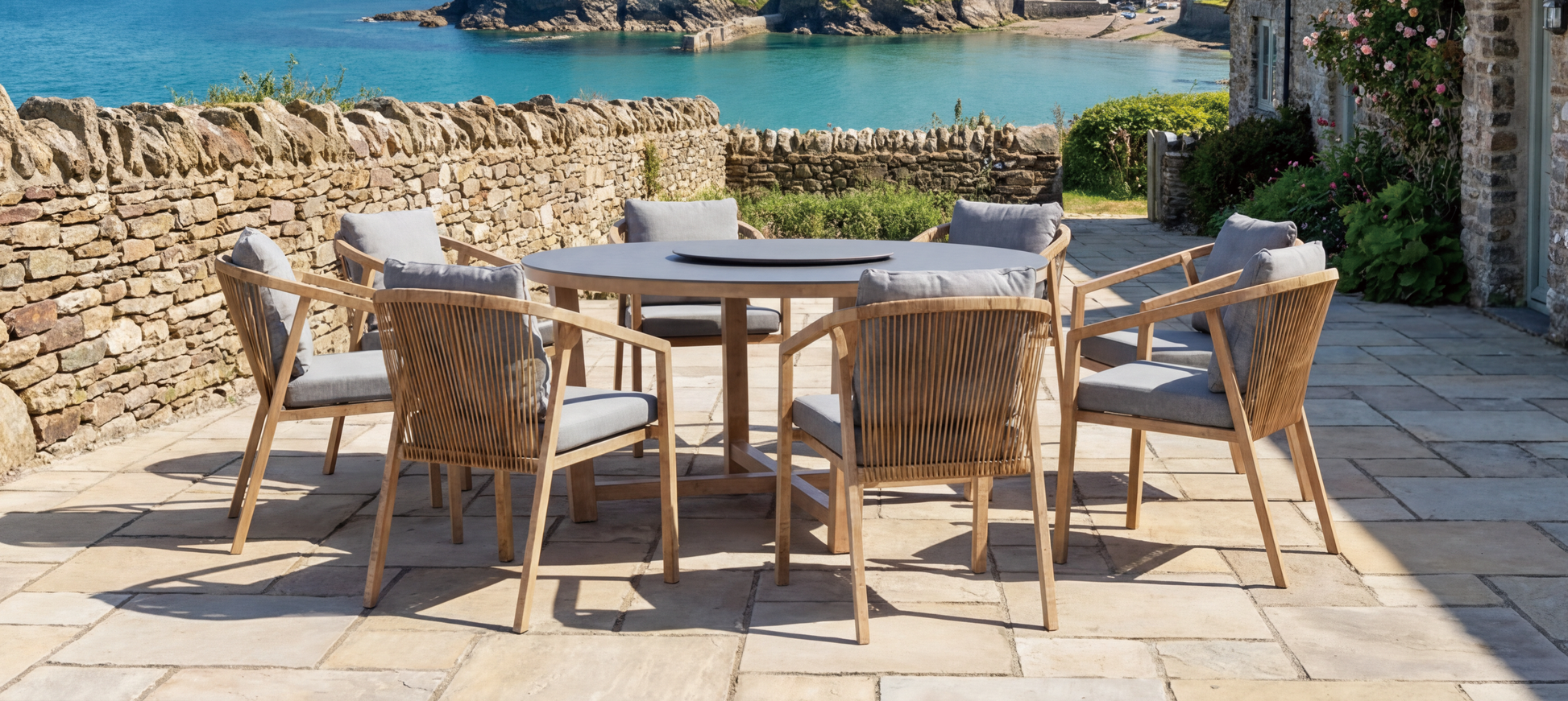 The Royal Garden Kanto Round Dining Set features a dark grey table top and light wooden frame with 8 matching rope detail chairs with cushions