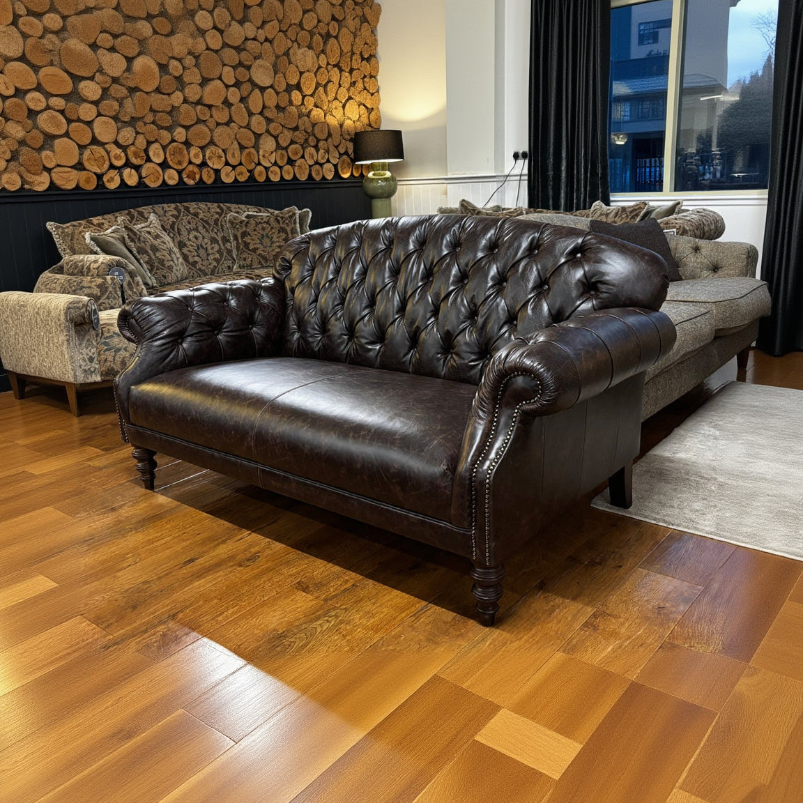 The Tetrad Arbroath Petit Sofa is crafted from genuine dark brown full grain leather with a deep diamond button tufting on the back and the scrolled arms, with brass stud detailing and elegant dark wood legs