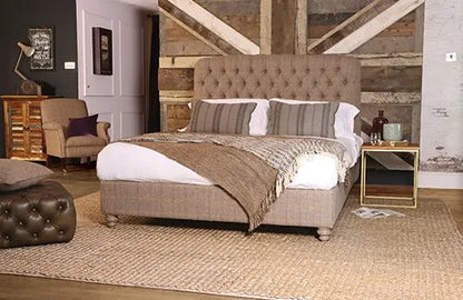 The Tetrad Berneray King Size Bed Frame is fully upholstered in Bracken Herringbone weave fabric, with a deep button tufted headboard and traditional turned feet