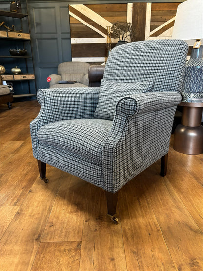 Tetrad Bowmore armchair handcrafted in Ebony Hounds Harris Tweed, a classic houndstooth check in charcoal grey and cream tones, rolled arms, dark wood legs with brass castors to the front legs