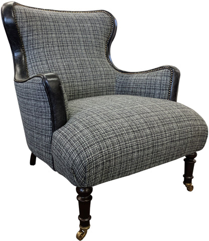 Tetrad Nairn Wing Chair in Mixed charcoal toned fabric with contrasting black Leather accents and brass stud detailing, with dark wood legs and front castors