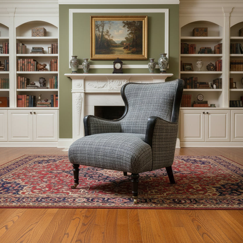 The Tetrad Nairn Wing Chair is upholstered in a mixed charcoal grey toned fabric with black Leather accents, dark wood legs and front castors