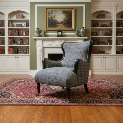 The Tetrad Nairn Wing Chair is upholstered in a mixed charcoal grey toned fabric with black Leather accents, dark wood legs and front castors