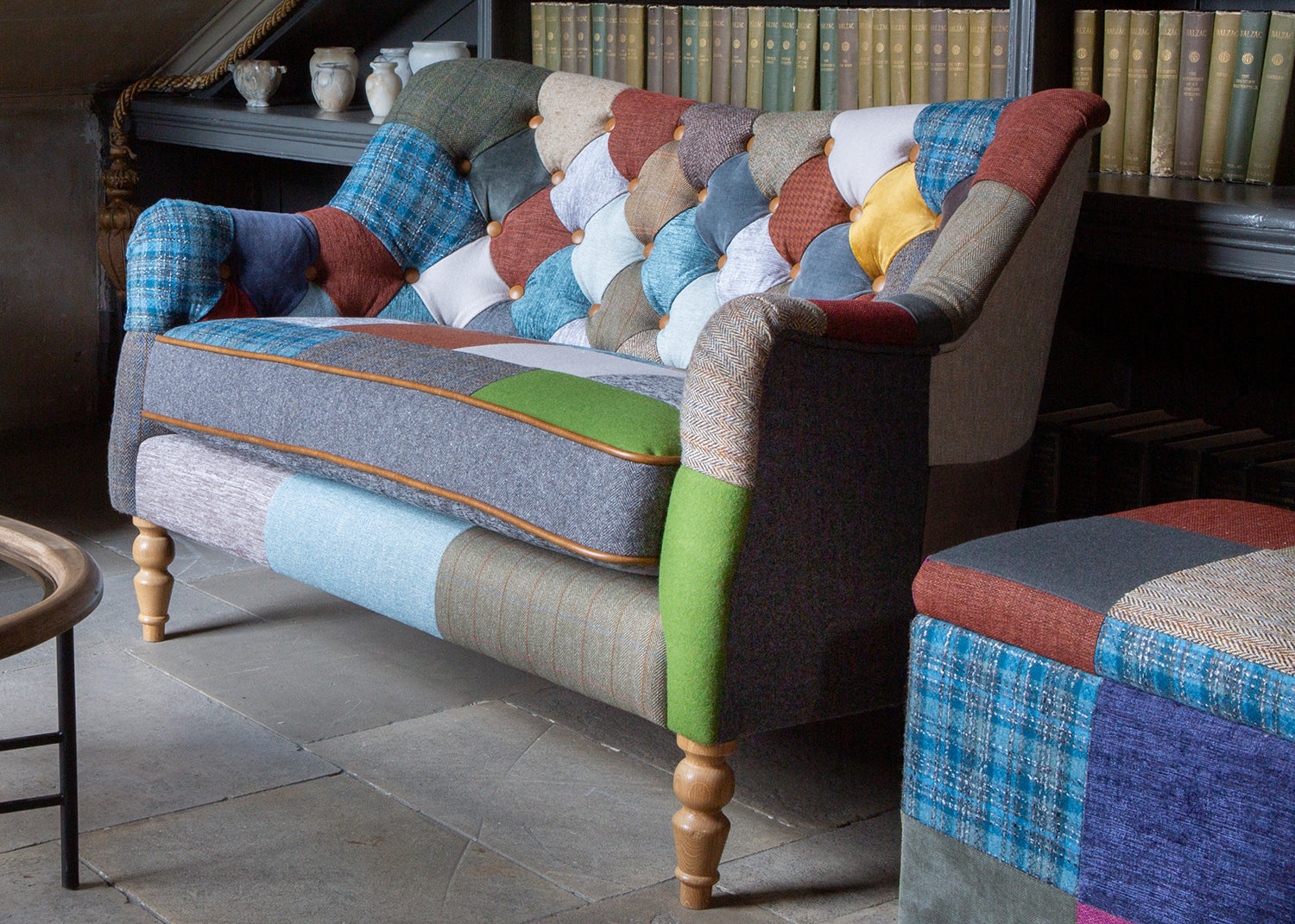 Vintage Sofa Company Alsace Patchwork Petit Sofa seats 2 people and features a generously padded seat cushion with tan leather trim, the backrest has deep button tufting with patchwork upholstery 