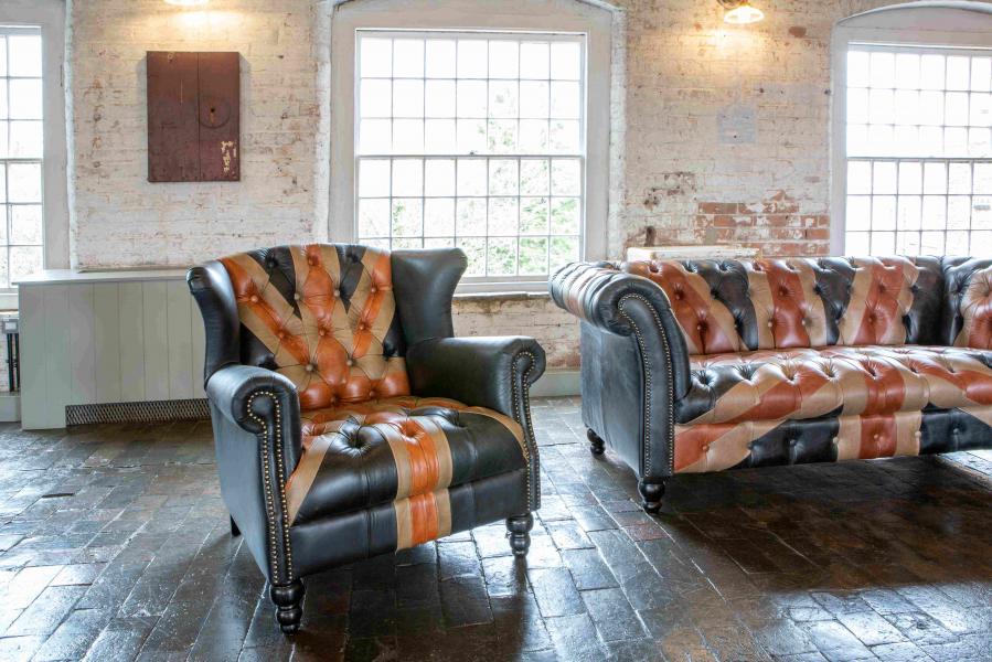 Vintage Sofa Company Crompton Union Jack Leather Statement Armchair features a high back, deep buttoning, navy, red and tan leather panels, studded scroll arms and turned wooden legs